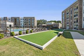 A grassy area in front of apartment buildings with a pool and a small pavilion.