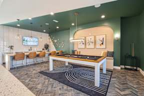 A billiard table is in the middle of a room, with a bard and TV behind.