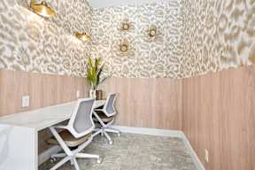 A room with a white desk and chairs with a patterned wallpaper.