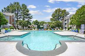 A large swimming pool in a residential area with trees and houses in the background.
