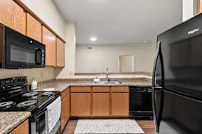 A kitchen with a black refrigerator and wooden cabinets.