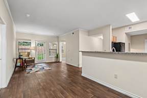 A spacious living room with hardwood floors and a kitchen area in the background.