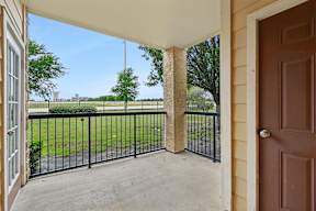 A view from a patio looking out to a green lawn and trees.