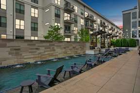 an outdoor pool with tables and chairs next to an apartment building