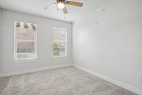 an empty room with two windows and a ceiling fan