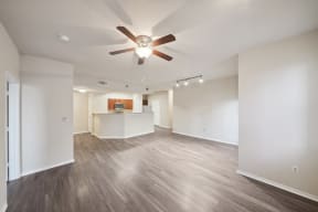 an empty living room with a ceiling fan and a kitchen