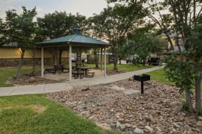 a gazebo in a park with benches and a grill