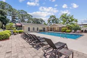 A poolside area with lounge chairs and a house in the background.
