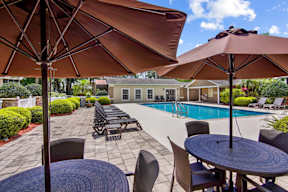 A patio with a table, chairs and umbrellas overlooking a pool.