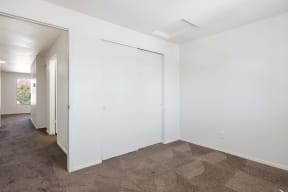 a living room with white walls and carpet and a door to a hallway