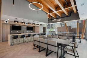 a communal area with tables and chairs and a kitchen with a bar and television