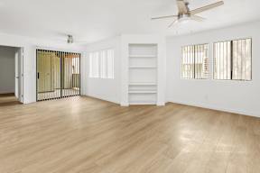 A room with a ceiling fan and light, hardwood floors, and a door with a gold-colored gate.