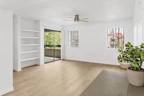 A room with a sliding glass door leading to a balcony, a ceiling fan, and a rug on the floor.