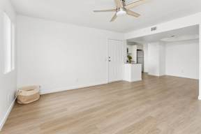 A room with a ceiling fan and light, hardwood floors, and a white door.