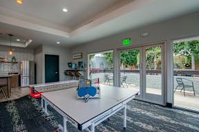 A ping pong table is in the middle of a room with a green exit sign on the wall.
