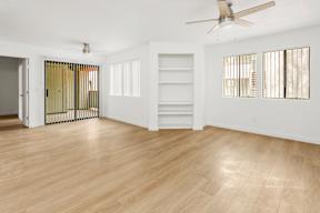 A room with a ceiling fan and light, hardwood floors, and a door with a gold-colored gate.
