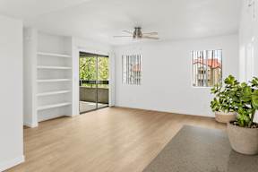 A room with a sliding glass door leading to a balcony, a ceiling fan, and a rug on the floor.