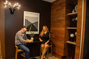 Two people sitting at a table in a room with a poster of the highway on the wall.