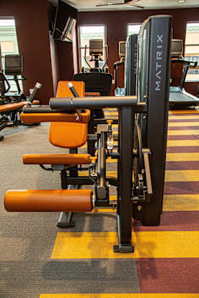 A gym with a row of orange chairs and a black weight machine.