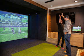 Two men playing a video game in a room with a green carpet.