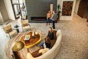 A group of people are sitting around a wooden coffee table in a spacious room.