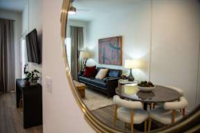 A living room with a black couch, a round table with four chairs, a television, and a large mirror.