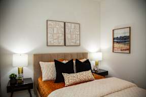 A bed with a white comforter and two black and white pillows is flanked by two lamps on either side.