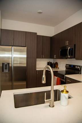 A kitchen with a stainless steel refrigerator and a black microwave above the stove.