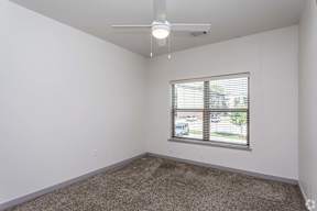 A room with a carpeted floor, a ceiling fan, and a window with blinds.