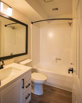 A white toilet is in a bathroom with a white tub and sink.