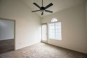 A room with a ceiling fan and two windows with blinds.