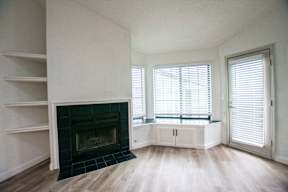 A fireplace with a black grate is in the middle of a room with a wooden floor and white walls.