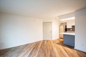 A room with a white door and a kitchen area with a refrigerator, sink and cabinets.