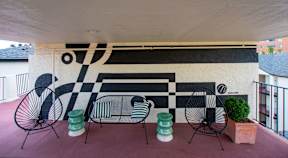 A black and white mural on a wall with a red couch and two chairs in front of it.