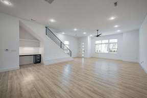 A spacious room with wooden flooring and a staircase.