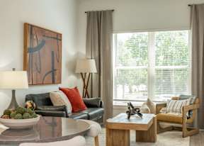 A living room with a black couch, a wooden coffee table, and a large window with blinds.