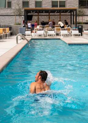 A man swims in a pool with people sitting on the poolside chairs.