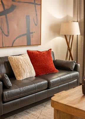 A black couch with a red pillow and a lamp on a wooden table.