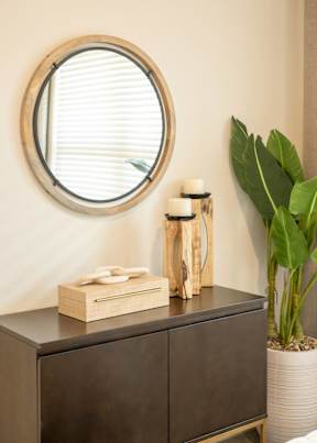 A round mirror with a wooden frame is on the wall above a wooden dresser.