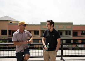 Two men are standing on a balcony, one is holding a bottle of water.