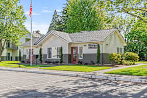 A building with a sign that says "LEASING OFFICE" is surrounded by trees and has a flagpole with an American flag in front of it.