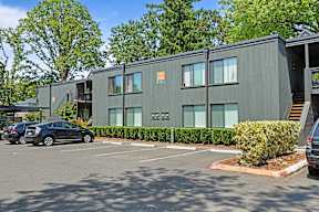 A grey building with a parking lot in front of it.