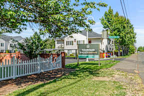 A sign for Fountain Valley Apartments stands in front of a white picket fence.