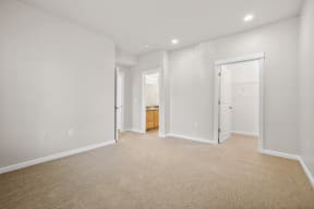 a living room with white walls and carpet and a door to a bathroom