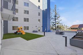 A playground area with a slide and a tree in front of a building.