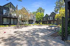 A sunny day at a courtyard with wooden benches and buildings in the background.