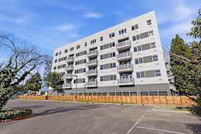 A large grey apartment building with a parking lot in front.