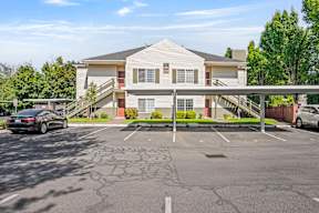 A car is parked in a parking lot in front of a two-story building.