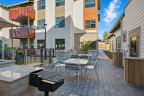 A patio with a grill and chairs is surrounded by apartment buildings.