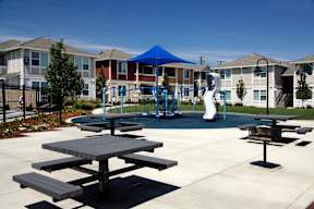 an outdoor playground with picnic tables in front of apartment buildings